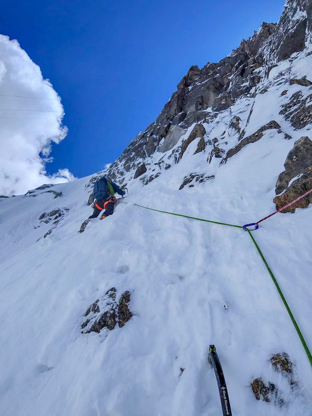 Un alpinista sale in cordata un pendio di neve e roccia