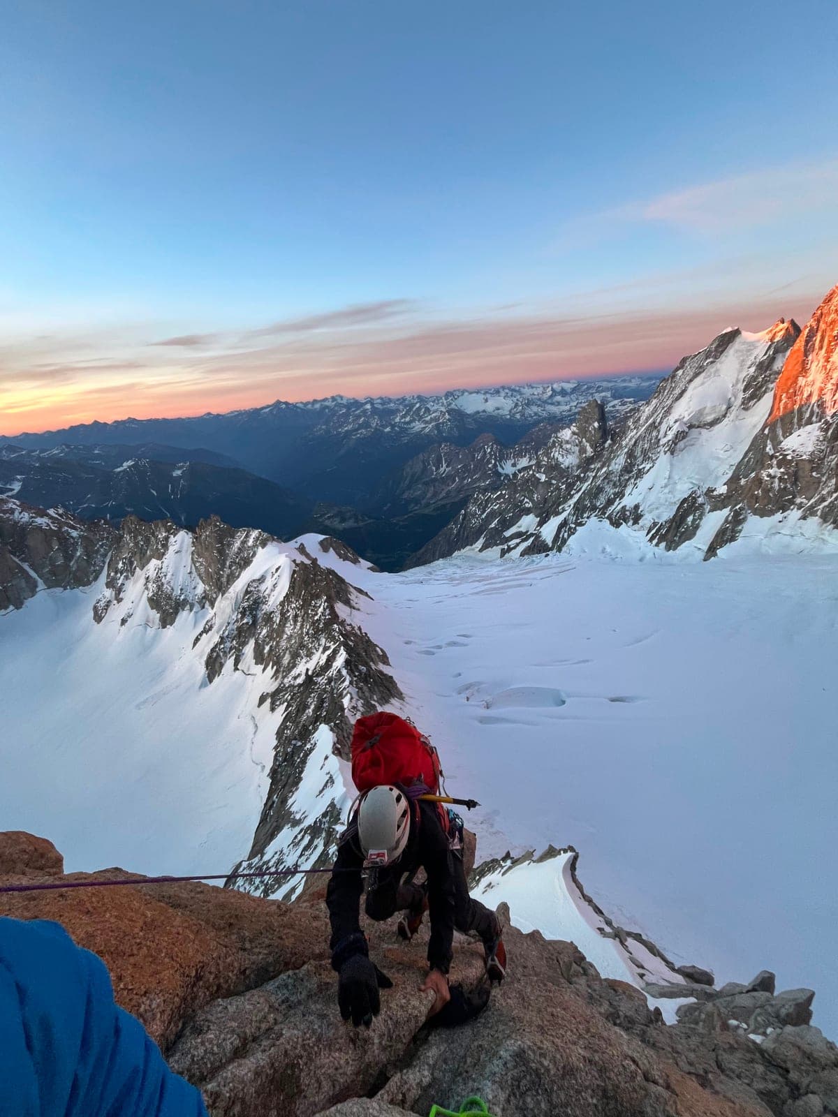 Un alpinista sale una cresta di roccia all'alba, sopra un ghiacciaio